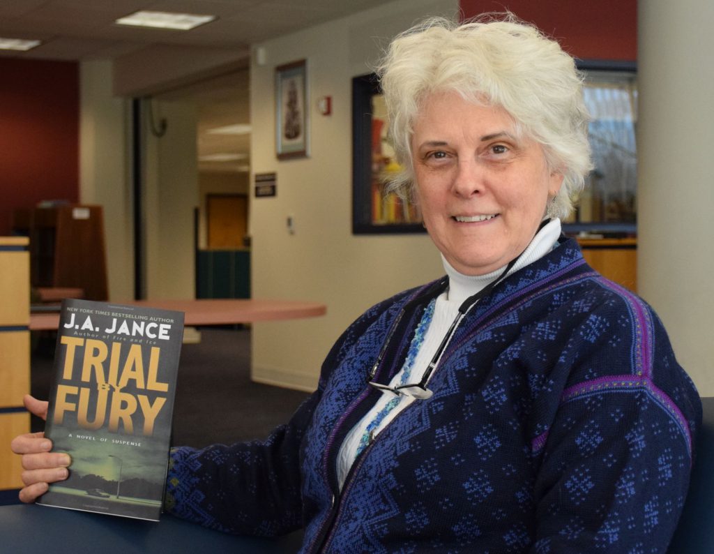 Outreach librarian Amy Ravenholt, holding the book Trial by Fury by J.A. Jance.