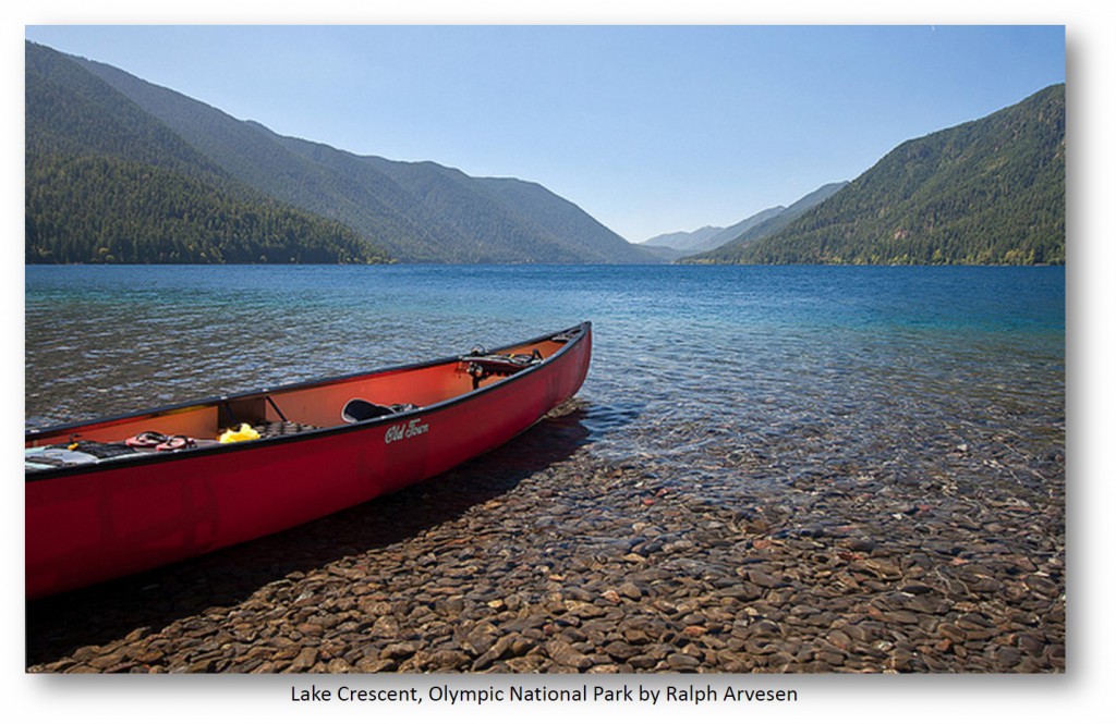 a red canoe on the shores of Lake Crescent in the Olympic National Park. Mountains in the distance.