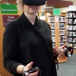 A woman with a VR headset and controls on her hands. The background is a library.